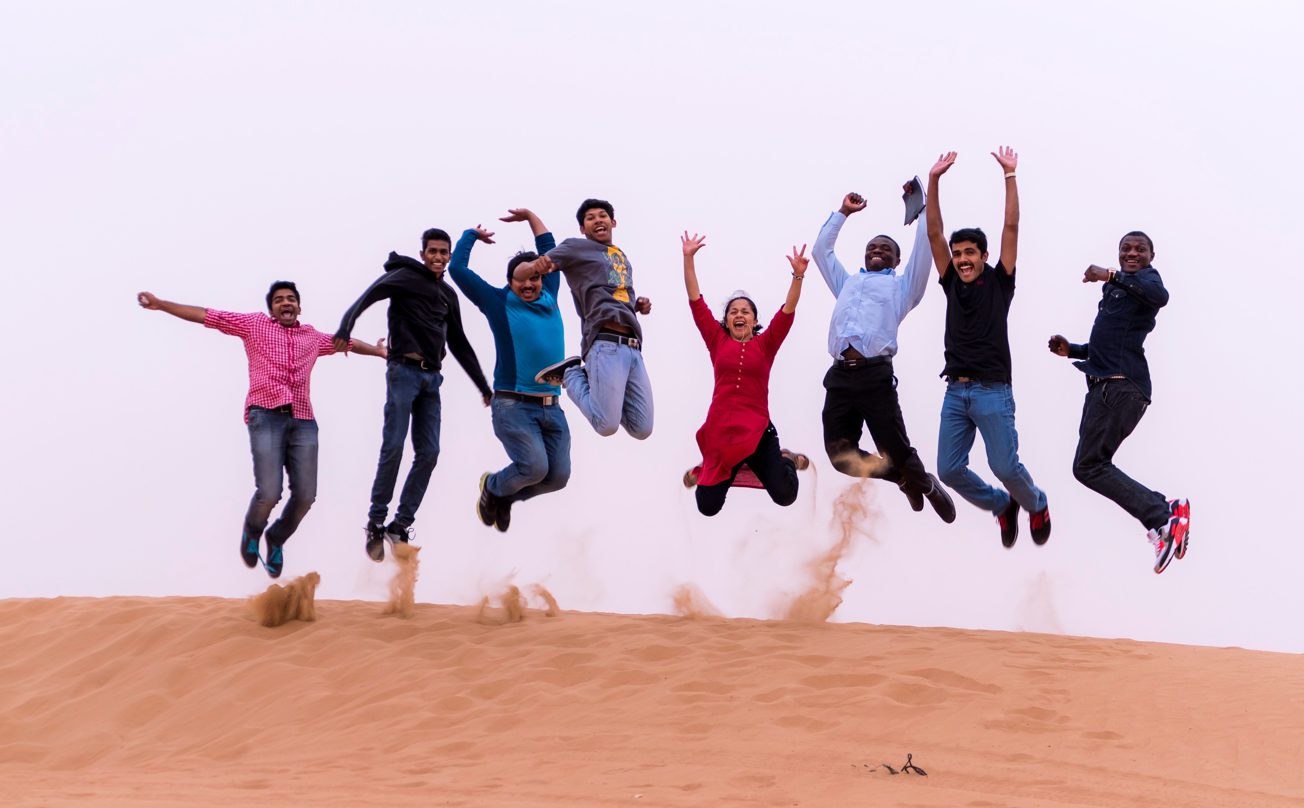 group of people jumping on sand dune